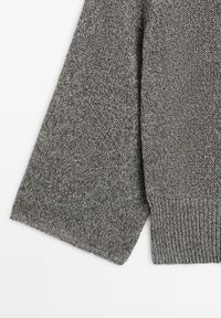 Manche de pull en maille grise avec bord-côte, posée à plat sur fond blanc, montrant la texture et les détails du tissu.