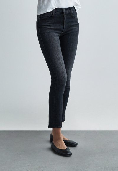 Jeans skinny neri a vita alta con una texture liscia, caratterizzati da un classico design a cinque tasche e un leggero effetto sbiadito, abbinati a ballerine nere.