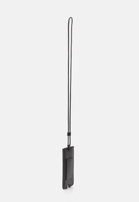 Tarjetero de cuero negro con una correa ajustable y fija. Presenta una superficie texturizada y un diseño recortado en la parte inferior. Forma simple y moderna.