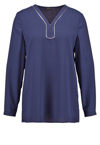 Blouse bleu marine à manches longues avec col en V et détails en piping blanc autour du col et de la poitrine.