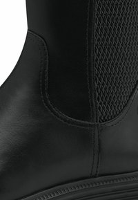 Black leather boot with textured mesh side panel, smooth finish, reinforced stitching, and a rounded toe design. Subtle tonal accents.