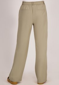 Beige wijde broek met elastische tailleband en paspelzakken, gedragen met bruine platte schoenen, gezien van achteren op een neutrale achtergrond.