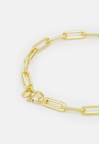 Bracciale in oro con anelli allungati, finitura lucida e chiusura circolare con un piccolo tag inciso per dettagli.
