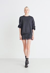 Tmavosivý oversize sveter s rolovanými rukávmi, kombinovaný s krátkou kockovanou sukňou; model má na sebe čierne členkové topánky. Jednoduchý dizajn a voľný strih.