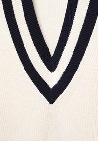 Tissu en tricot blanc avec un décolleté en V profond bordé de rayures côtelées alternant noir et blanc.