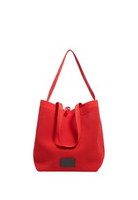 Rode mesh tote bag met verstelbare schouderbanden, een ronde vorm en een zwarte rechthoekige label. Heeft een trekkoordsluiting aan de bovenkant.