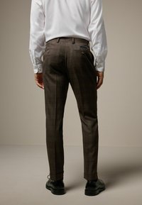 Pantaloni cu carouri maro, dintr-un material texturat, având un croi slim, cu buzunare laterale și buzunare decorative la spate, asortați cu pantofi negri.