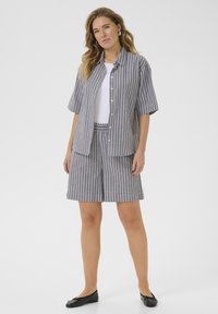 Chemise à manches courtes rayée et short assorti en gris avec des rayures blanches. Le matériau semble léger ; la chemise possède des boutons, le short a une taille élastique.
