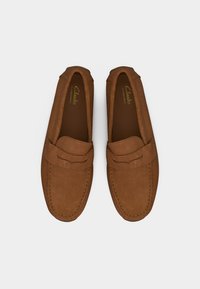 Paire de mocassins penny en daim marron avec couture visible, semelle plate, et logo Clarks Signature à l'intérieur de chaque chaussure.