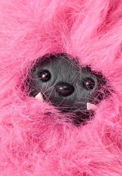 Visage de jouet noir avec des yeux ronds et un nez, petites crocs blanches, entouré d'une fourrure rose vif et duveteuse.