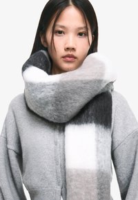 Scialle oversize grigio e bianco realizzato in morbido lana, caratterizzato da un motivo geometrico con passaggi di colore graduali e una texture soffice.