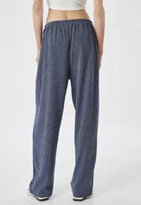 Pantalons larges en bleu texturé avec une taille élastique, présentant une coupe ample et de subtiles rayures verticales. Pas de poches ni de métal visibles.