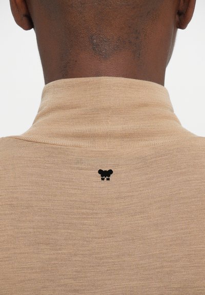 Pulover bej cu guler înalt, cu o textură textilă crestată; are un logo mic negru în partea de sus a spatelui, aproape de guler.