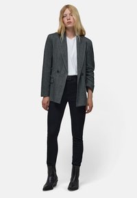 Blazer de cuadro gris de doble botonadura con mangas largas, combinado con una camiseta blanca y jeans skinny negros, acentuado por botas negras hasta el tobillo.