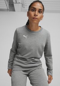 Felpa grigia con maniche lunghe, colletto a coste e orlo elasticizzato. Presenta un logo Puma bianco sul lato sinistro del petto. Tessuto morbido.
