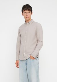 Svetlosivá košeľa s dlhým rukávom a golierom, s textúrovanou tkaninou a slim fit strihom, nosená s svetlomodrými džínsami.