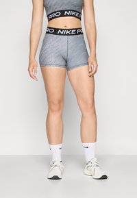 Dvoukusová sada Nike Pro skládající se ze šedé sportovní podprsenky a odpovídajících šortek s černým elastickým pasem s bílým logem, přiléhavý design.