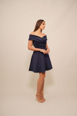 Navy blue off-the-shoulder dress with a fitted bodice and flared skirt. Smooth fabric with a draped neckline and subtle sheen. Tan strappy heels.