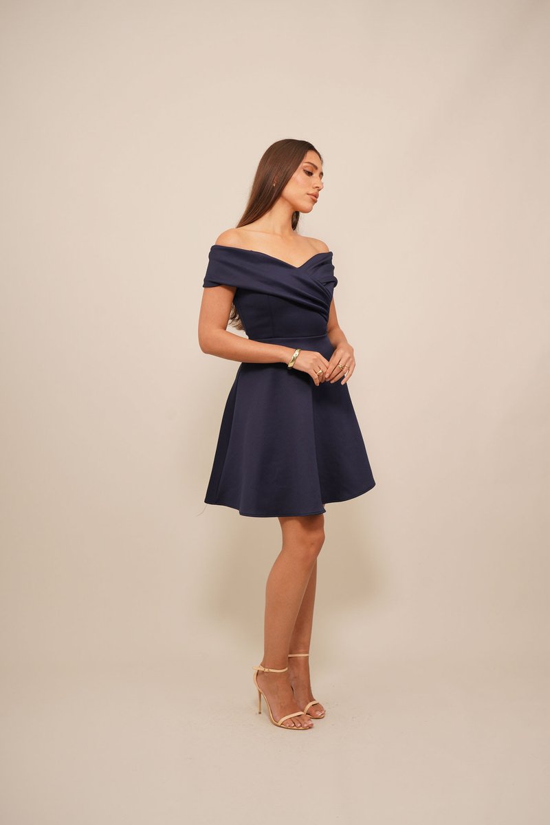 Abito blu navy con spalle scoperte, con corpino aderente e gonna a ruota. Tessuto liscio con scollatura drappeggiata e leggera lucentezza. Tacchi a strappo color sabbia.