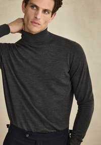 Mörkgrå polotröja i mjukt och glatt tyg. Har långa ärmar och en figurnära design, kombinerad med mörka byxor.