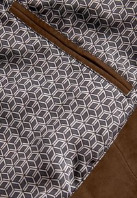 Tejido de patrón geométrico en gris y blanco con acentos de ante marrón. Presenta un diseño de diamante y cubo, textura suave y costuras precisas.