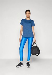 Camiseta deportiva azul, leggings azules brillantes, zapatillas deportivas negras y una bolsa de gimnasio negra, presentados sobre un fondo gris claro.