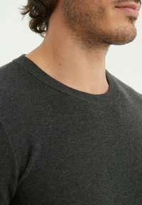 Pull en maille gris foncé avec un col rond, mettant en valeur un tissu texturé. La coupe semble normale, avec un design simple et sans motifs visibles.