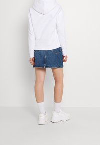 Sudadera blanca con capucha combinada con una falda de mezclilla, con un dobladillo deshilachado y dos bolsillos traseros. Llevada con zapatillas blancas y calcetines.