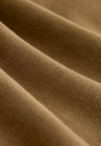 Brown fabric with a soft, textured surface, featuring fine knit patterns and subtle variations in shade across the folds.