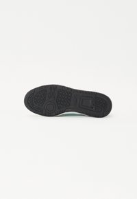 Semelle de chaussure en caoutchouc noir avec un motif de semelle, finition texturée et une touche de vert lisse près du bord.