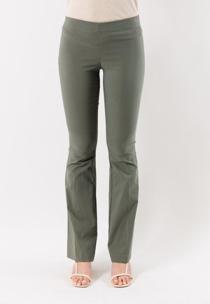 Pantaloni verde oliva a vestibilità aderente con leggero svasamento alle caviglie, indossati con sandali beige aperti con tacco su uno sfondo neutro.