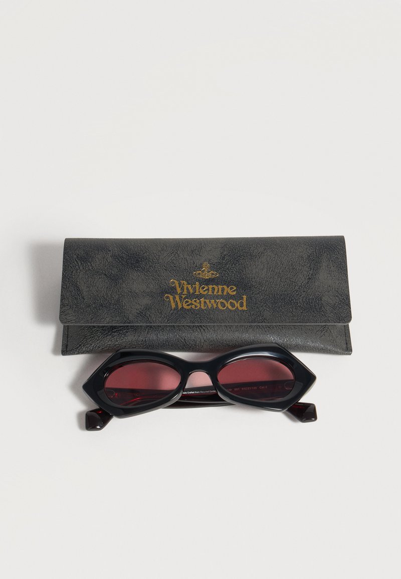 Black cat-eye sunglasses with dark red lenses placed in front of a black textured Vivienne Westwood branded case.