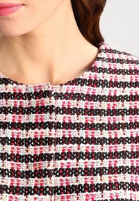 Un tissu en tweed texturé avec des rayures rose, noir et blanc, doté d'un col rond et d'une fermeture bouton discrète au niveau du col.