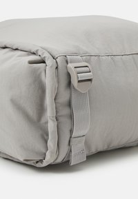 Cuscino grigio imbottito con una superficie in tessuto liscio, dotato di una tracolla laterale e una fibbia in plastica per un trasporto sicuro, forma squadrata e bordi cuciti.