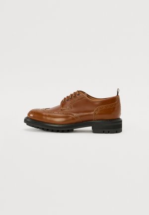 Chaussure oxford en cuir marron avec design à bouts relevés, bout rond, broderies détaillées et semelle en caoutchouc noire. Comprend un système de laçage et une languette.