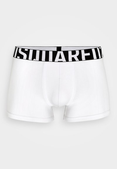 White cotton boxer shorts featuring a black elastic waistband with bold white branding. Smooth texture and fitted design.