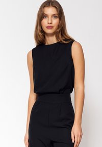 Czarny top bez rękawów z wysokim dekoltem i luźnym krojem, wykonany z gładkiego materiału. Połączony z czarnymi spodniami z wysokim stanem, o minimalistycznym designie.