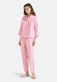 Conjunto de pijama a rayas rosas con una parte superior de botones de manga larga que presenta un cuello y pantalones con puños. Textura de tela suave y corte relajado.