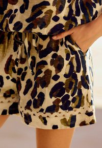 Leopardenmuster-Shorts in Beige mit blauen, braunen und grünen Spritzern. Sie verfügen über seitliche Taschen und einen Kordelzug mit dekorativen Nähten.