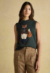 Zaļš bez piedurknēm džempers ar izšūtu lapsu žaketē, apvienots ar brūnām plākstera augstās vidukļa biksēm.