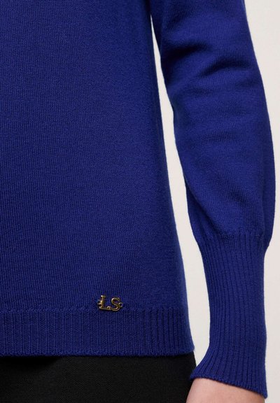 Royalblauer gestrickter Pullover mit geripptem Saum und Bündchen, versehen mit einem kleinen goldenen Logoakzent unten links. Weiche Textur, figurbetontes Design.