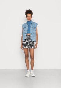 Gilet en denim à manches courtes sur un crop top en côtes bleu et un short à imprimé zèbre noir et blanc. Des baskets blanches complètent le look.