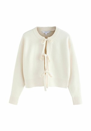 Kreminė megzta kardiganas su raukiniais ir trimis priekyje surišamais kaspinais, ilgomis rankovėmis ir sutrumpintu siluetu.