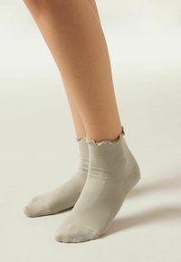Helle graue, gerippte Knöchelsocken mit einem gewellten oberen Rand, aus einem weichen Stoff gefertigt. Entworfen, um eng um den Fuß zu sitzen.