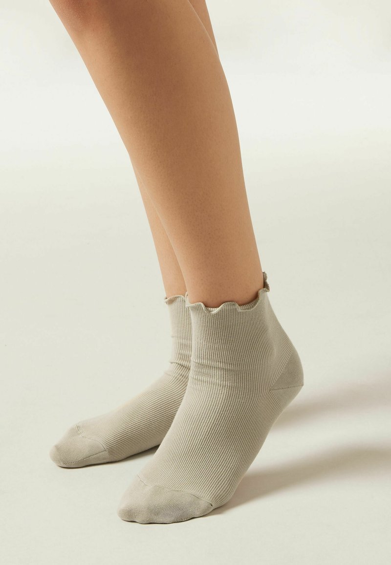 Calcetines de tobillo de color gris claro, con un borde superior con volantes, fabricados en un tejido suave. Diseñados para ajustarse cómodamente al pie.