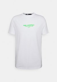 Camiseta de algodón blanca con cuello redondo y mangas cortas, que presenta un texto en verde neón que dice "KARL LAGERFELD 21 RUE ST-GUILLAUME PARÍS."