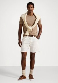 Rudos spalvos marškinėliai, balti džinsiniai šortai su neapdorotu kraštu, kreminės spalvos megztinis, rišamas aplink kaklą, rudi sportbačiai ir smėlio spalvos kojinės. Kasdienis vasaros stilius.