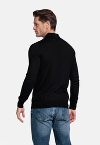 Zwarte gebreide pullover met lange mouwen en een kraag. Draag het met lichtblauwe jeans, gemaakt van een gestructureerde stof met een slim-fit silhouet.