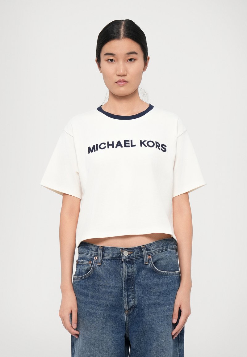 T-shirt bianco a croppato con colletto blu navy e logo "MICHAEL KORS" in blu scuro. Abbinato a jeans in denim blu a vita alta.