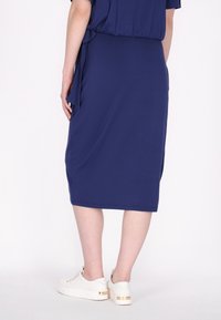 Marineblauwe midi-jurk van zachte stof, met een gestrikte taille, een gladde textuur en gecombineerd met witte sneakers met gouden accenten.